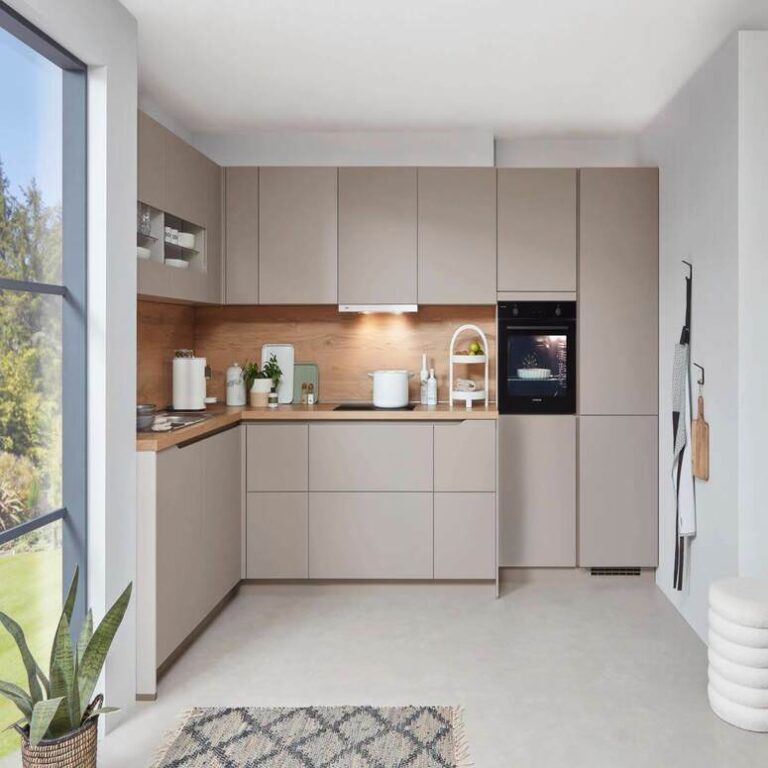 Musterküche in Kaschmir als L-Küche mit Holzrückwand und Backofen im Hochschrank – Küchenstudio Leverkusen